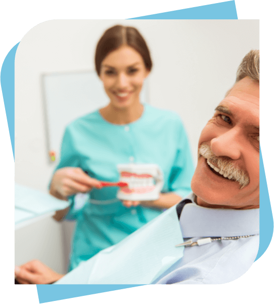 Man with a moustache smiling while the hygienist shows proper brushing technique on a model.