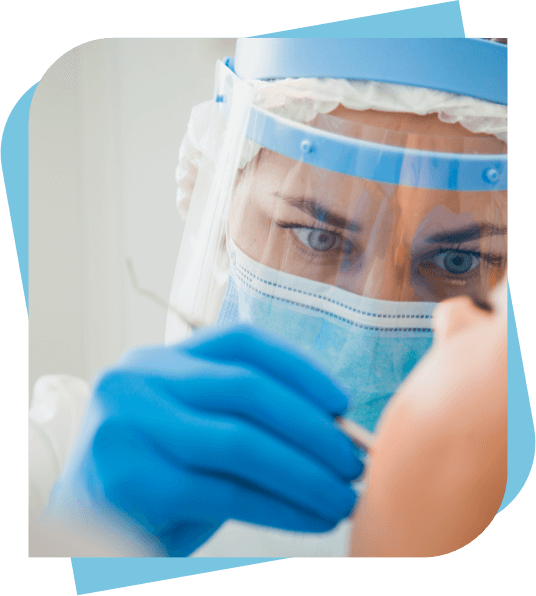 Dentist with a mask and face shield working on a patient's mouth.