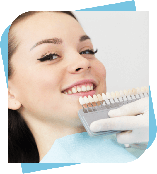 Woman smiling while a dentist checks tooth colour with a display of veneers.