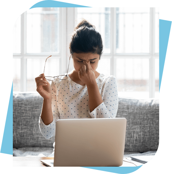 Woman sitting at her laptop holding her glasses and pinching the bridge of her nose.