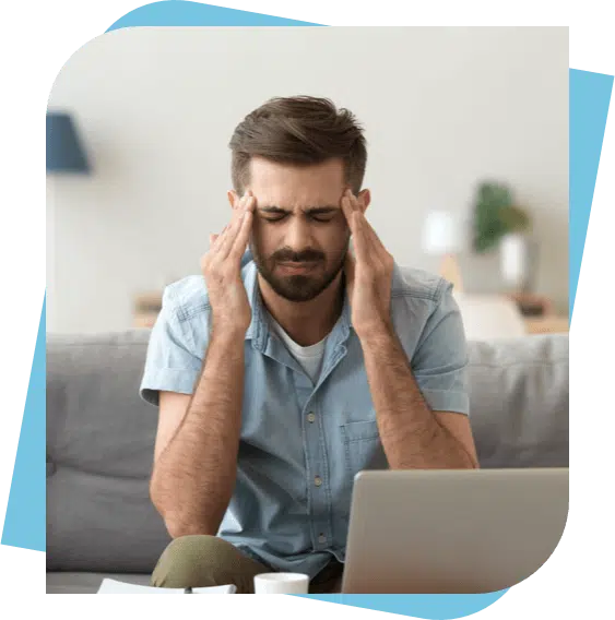 Man sitting in front of his laptop on a couch massaging his head to relieve migraine pain.