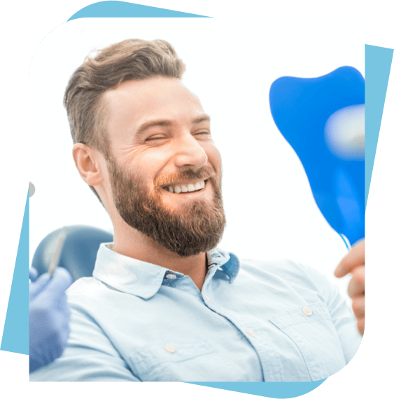 Man with a beard sitting in a dental chair looking at his smile in a mirror.