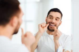 man looking in mirror as he flosses his teeth