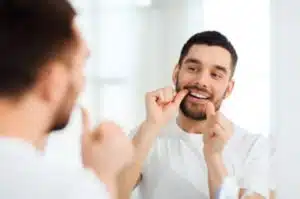 man looking in mirror as he flosses his teeth